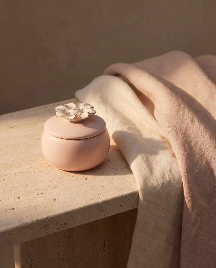 A sculptural pink ceramic flower candle resting on a travertine ledge in warm dusk light.