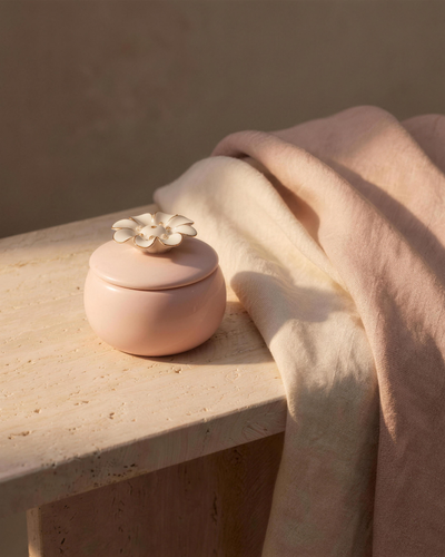A sculptural pink ceramic flower candle resting on a travertine ledge in warm dusk light.