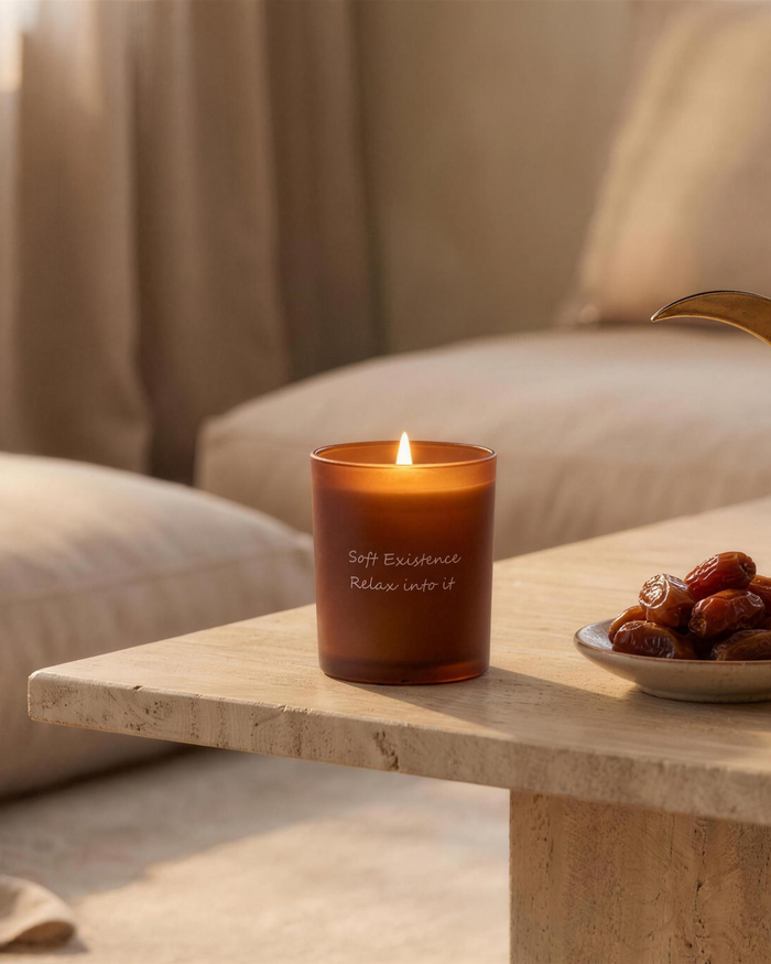 Calm modern majlis styled for Ramadan with a lit Soft Existence amber candle, a dish of dates and a brass Arabic coffee dallah