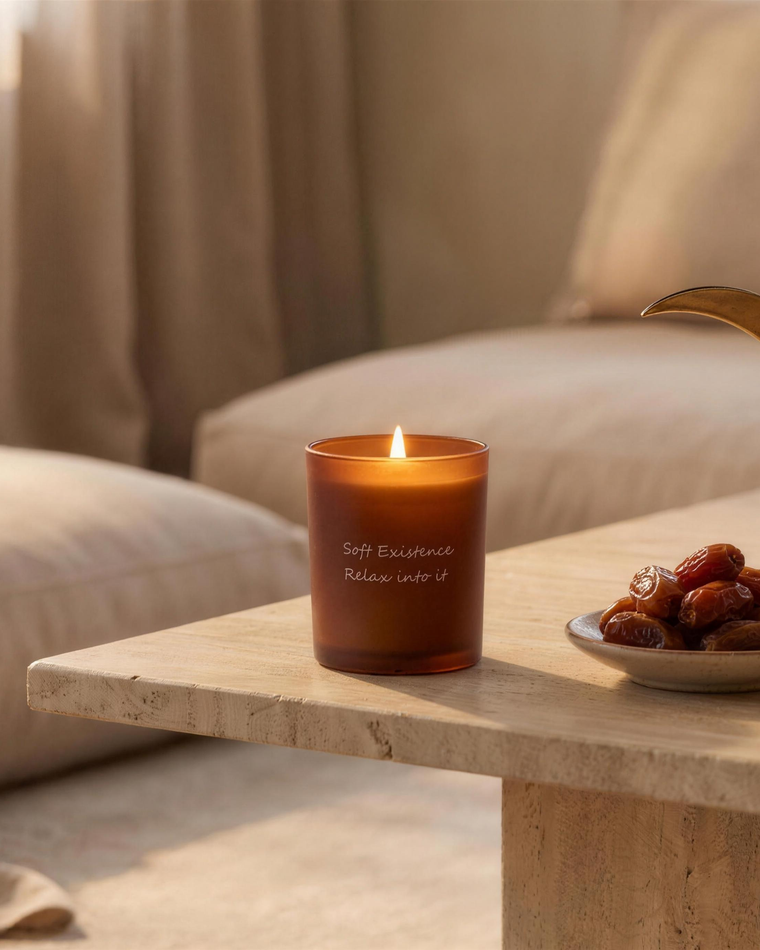 Calm modern majlis styled for Ramadan with a lit Soft Existence amber candle, a dish of dates and a brass Arabic coffee dallah