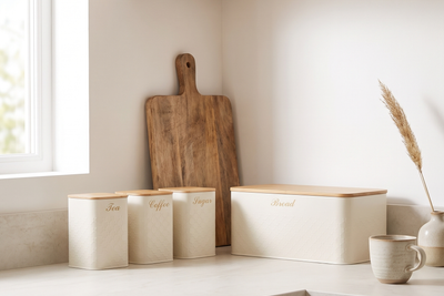 Scandinavian-style kitchen with pale oak cabinets and a light stone counter, a cream four-piece canister and bread bin set with bamboo lids in a row against the wall, a wooden board leaning behind and a ceramic cup