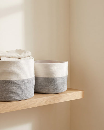 White and grey hand-woven cotton storage baskets holding folded linen on an oak shelf