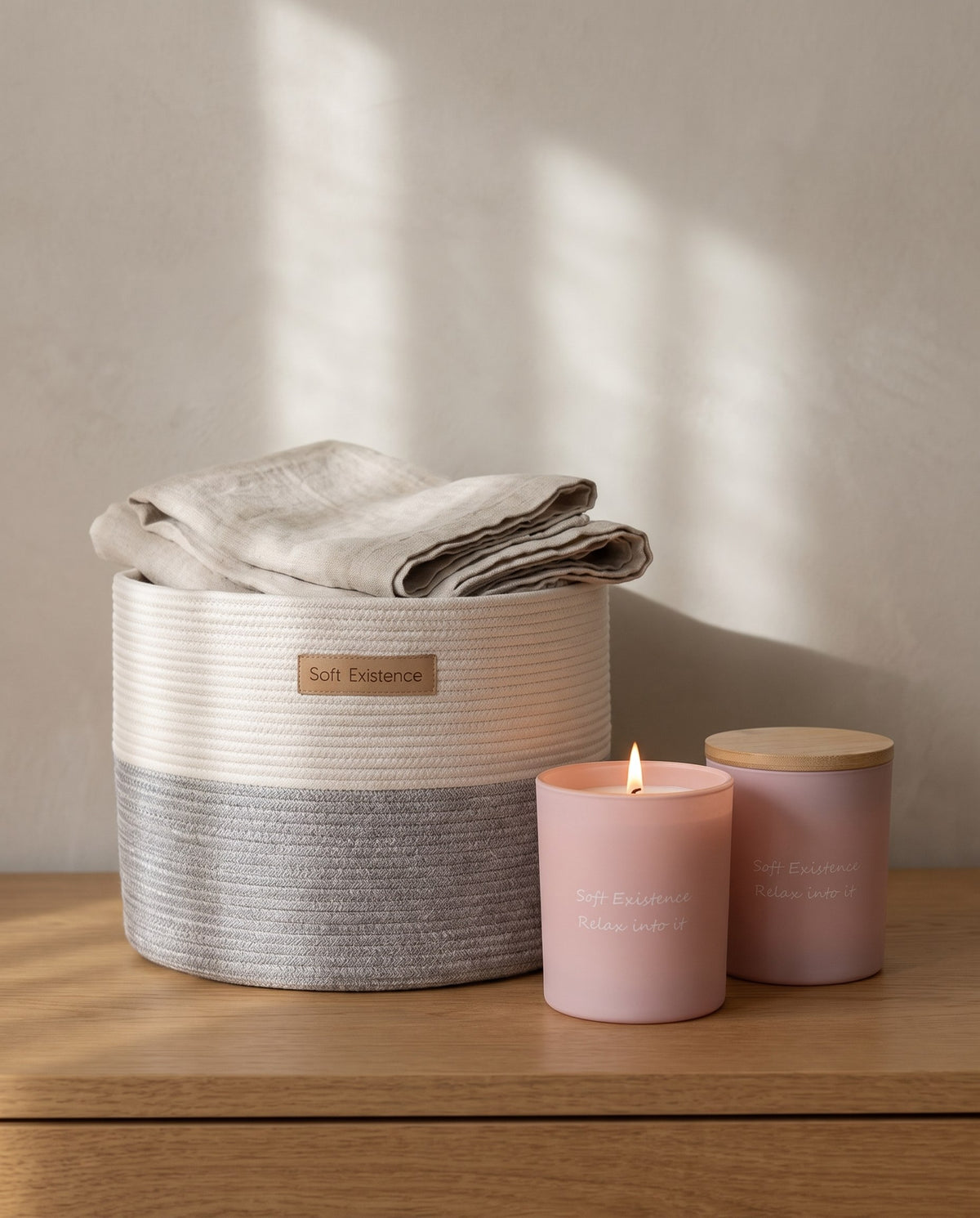 Hand-woven cotton basket with folded linen beside lit blush soy candles